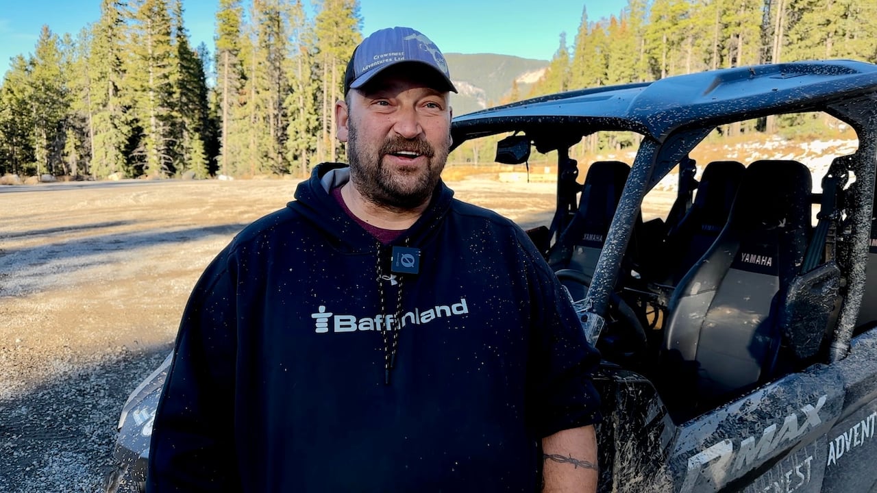 A man in a black hoodie gives an interview in front of a black SUV.