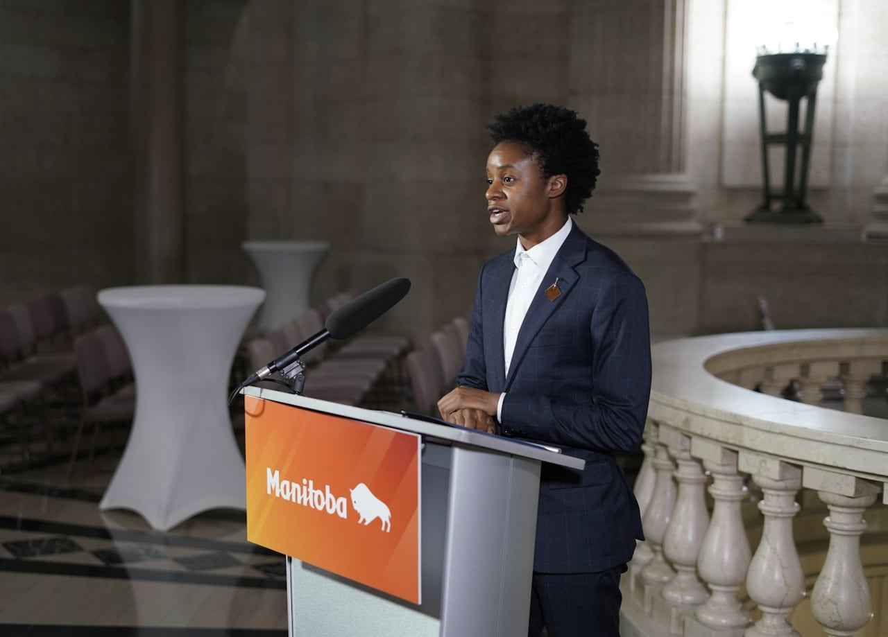 A person in a dark suit and white shirt speaks into a microphone at a lectern.