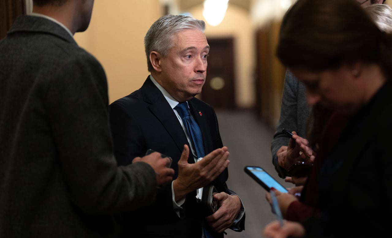 A man gestures with his hand while talking to a group of people holding phones and recording devices.
