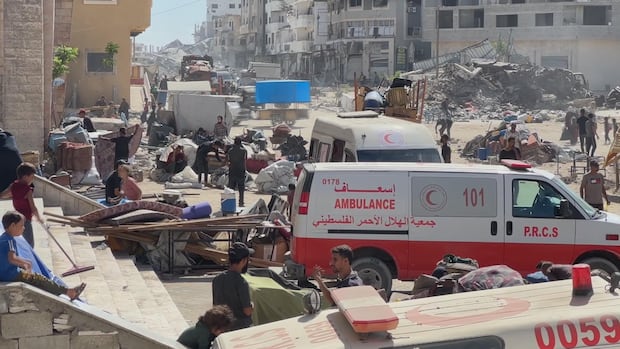 Ambulances and people are gathered on the front stone steps of a building. Furniture and belongings are sitting in piles.