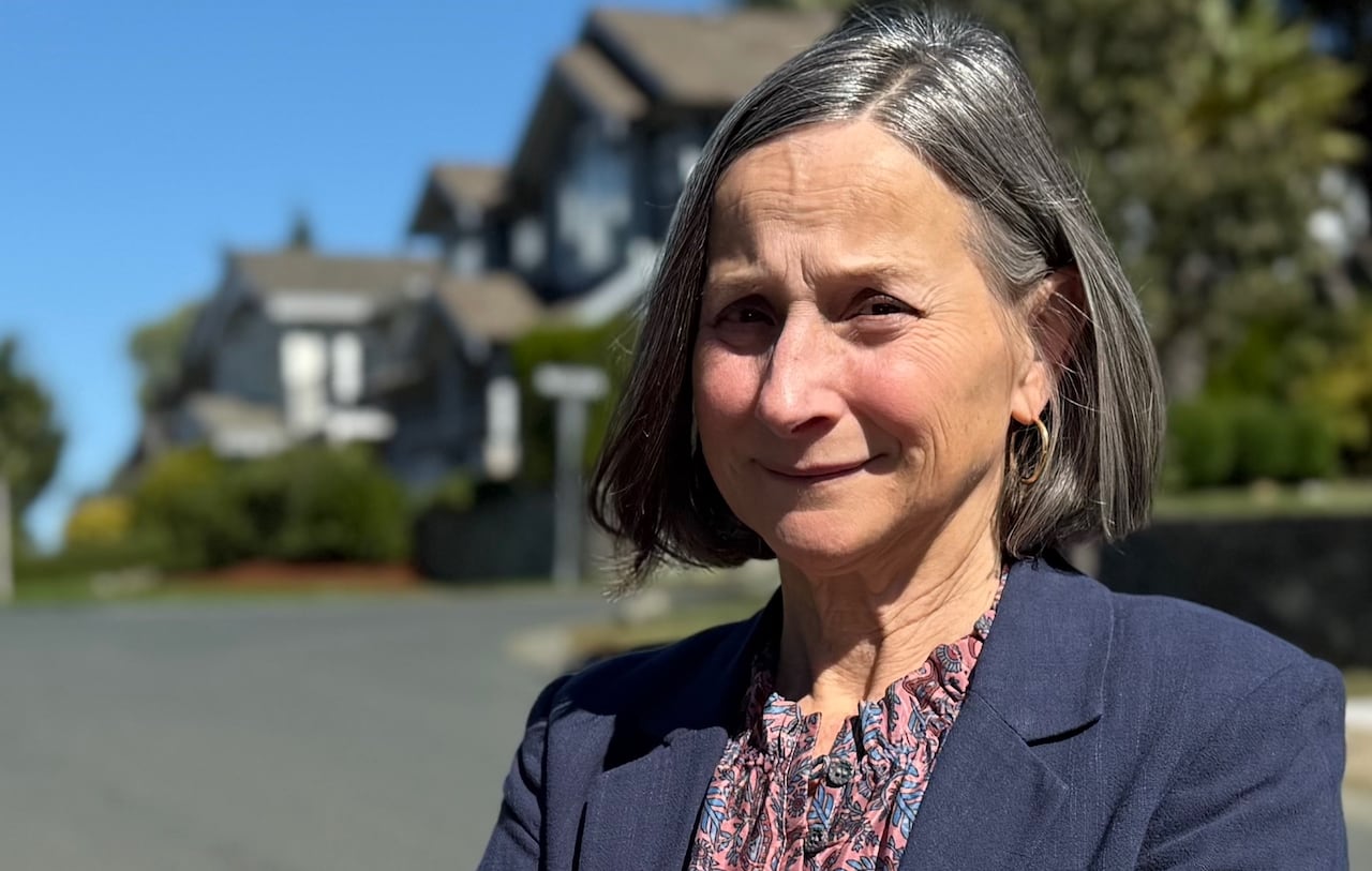 A woman standing on the side of a residential street looks into the camera