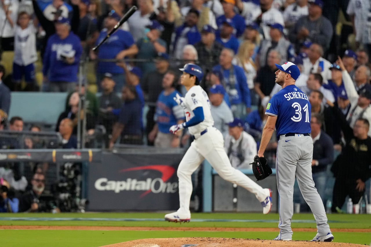 Dodgers' Shohei Ohtani tosses his bat as Blue Jay Max Scherzer looks toward the outfield wall at Dodger Stadium after Ohtani hit a home run in Game 3 of the World Series. The blurred crowd in the background is standing and cheering