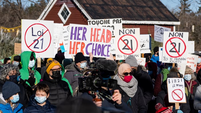 Demonstrators hold signs condemning Bill 21 in front of an elementary school
