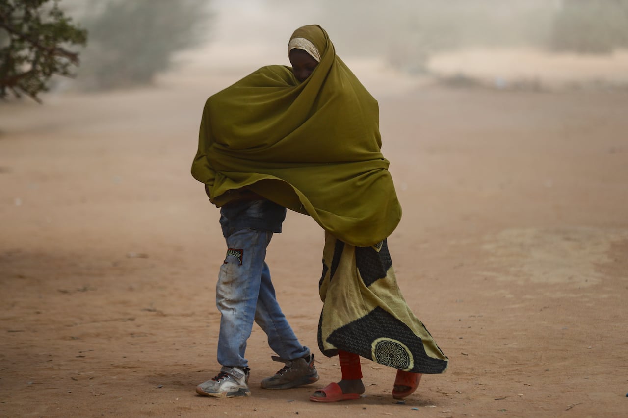 Children cover themselves with a blanket as they walk along the dusty road.