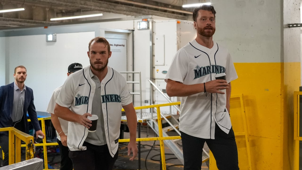 Two men wearing Seattle Mariners jerseys walking into an arena.