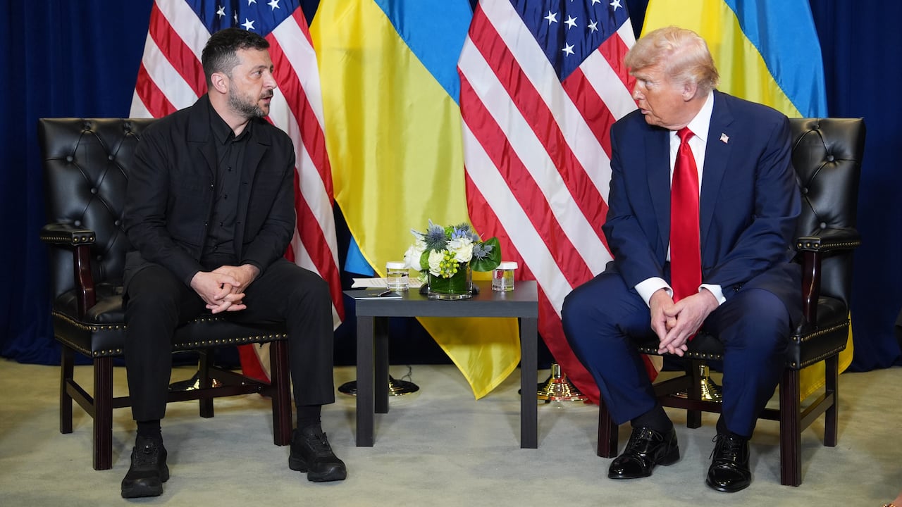Trump and Zelenskyy, seated in chairs with a backdrop of the Ukraine and U.S. flags, lean toward each other in conversation. 