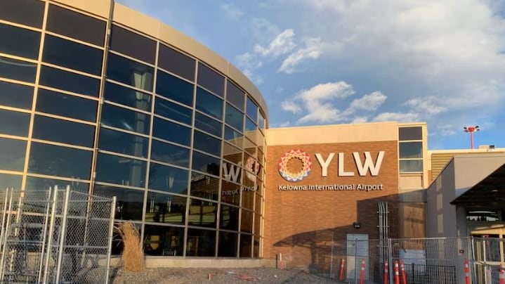 The exterior of a stone and glass building with a sign reading, 'YLW Kelowna International Airport.'