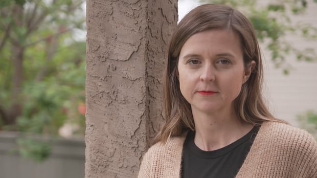 Registered nurse Ashley Stone has worked in healthcare in B.C.'s Interior for 16 years, and for the last 11 she's also been battling repeated cases of her identity being stolen. A woman wearing a beige cardigan leans against a post and looks straight on.