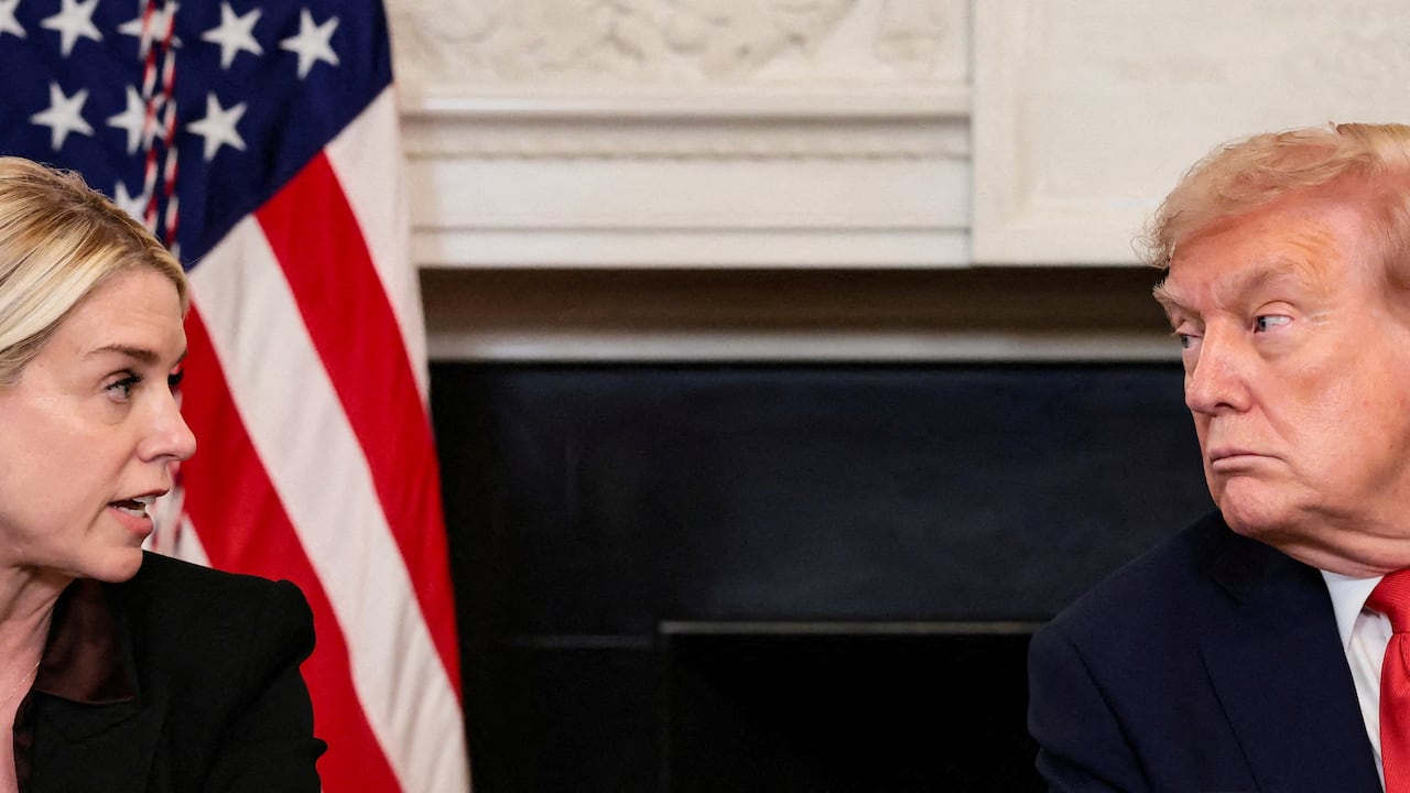 A man and a woman have a conversation seated in front of an American flag