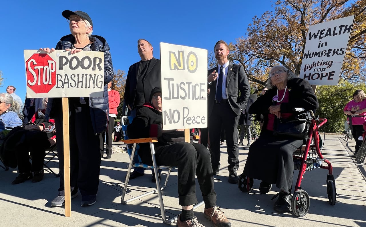 A person holds a sign that says "Stop poor bashing" and another sign says "no justice no peace"