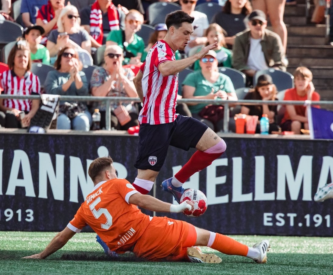 One soccer player jumps over another who's trying a slide tackle.