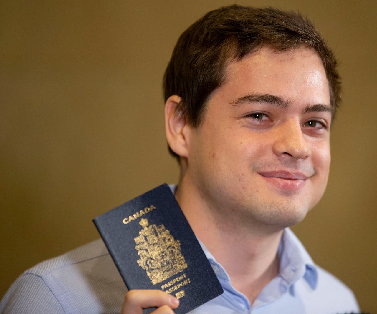 A man holds up a passport and smiles.