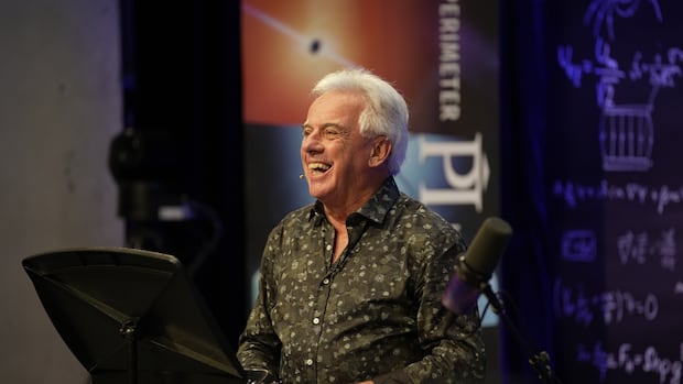 Bob McDonald looks at the audience during a recording of Quirks & Quarks at the Perimeter Institute in Kitchener, Ont. A man with white hair looks off camera, smiling broadly. Microphones are seen in the foreground.