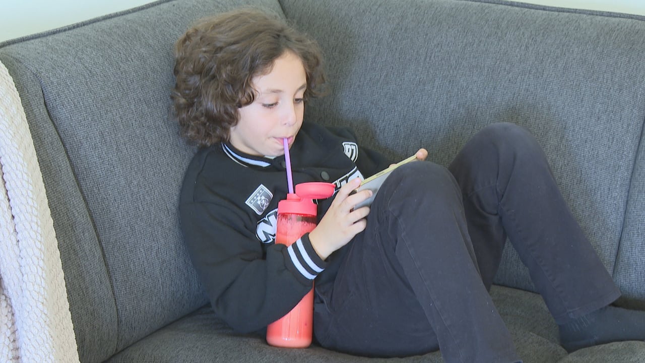 A boy sits on a couch drinking a smoothie.