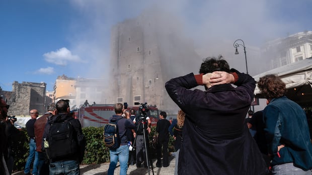 Onlookers watch as dust rises after the partial collapse of a building.
