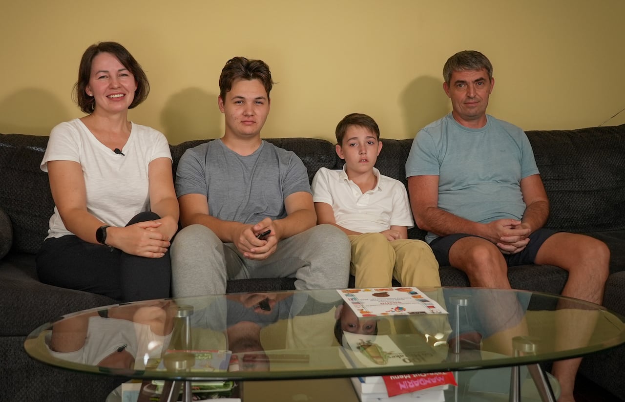 Una familia de cuatro miembros, entre ellos una madre, un padre y dos hijos, está sentada en un sofá de una sala de estar.