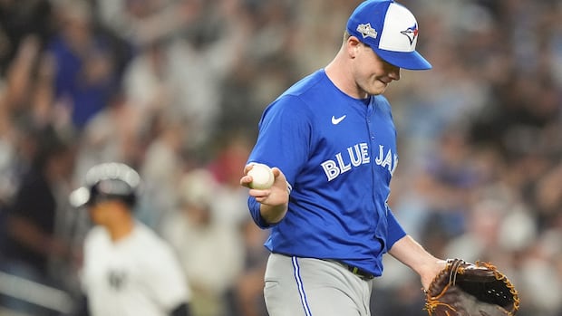 A pitcher in a Blue Jays jersey goes to throw a baseball in his mitt and he looks down.