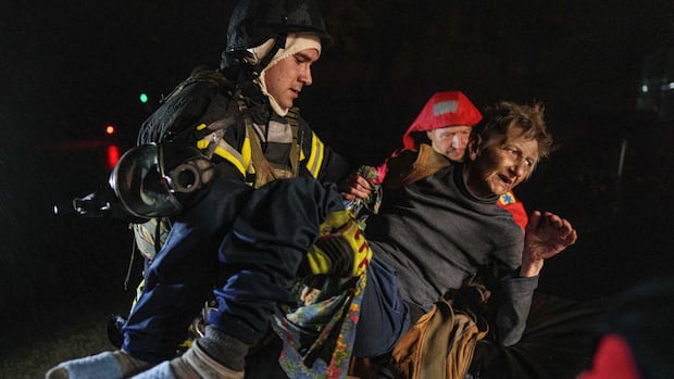 Rescuers carry an injured woman into an ambulance after a Russian strike on a residential neighborhood in Kyiv, Ukraine, on Friday, Oct. 10, 2025. (AP Photo/Evgeniy Maloletka) An older woman wearing a turtleneck and jeans and slippers is carried by a hooded firefighter in a nighttime scene.
