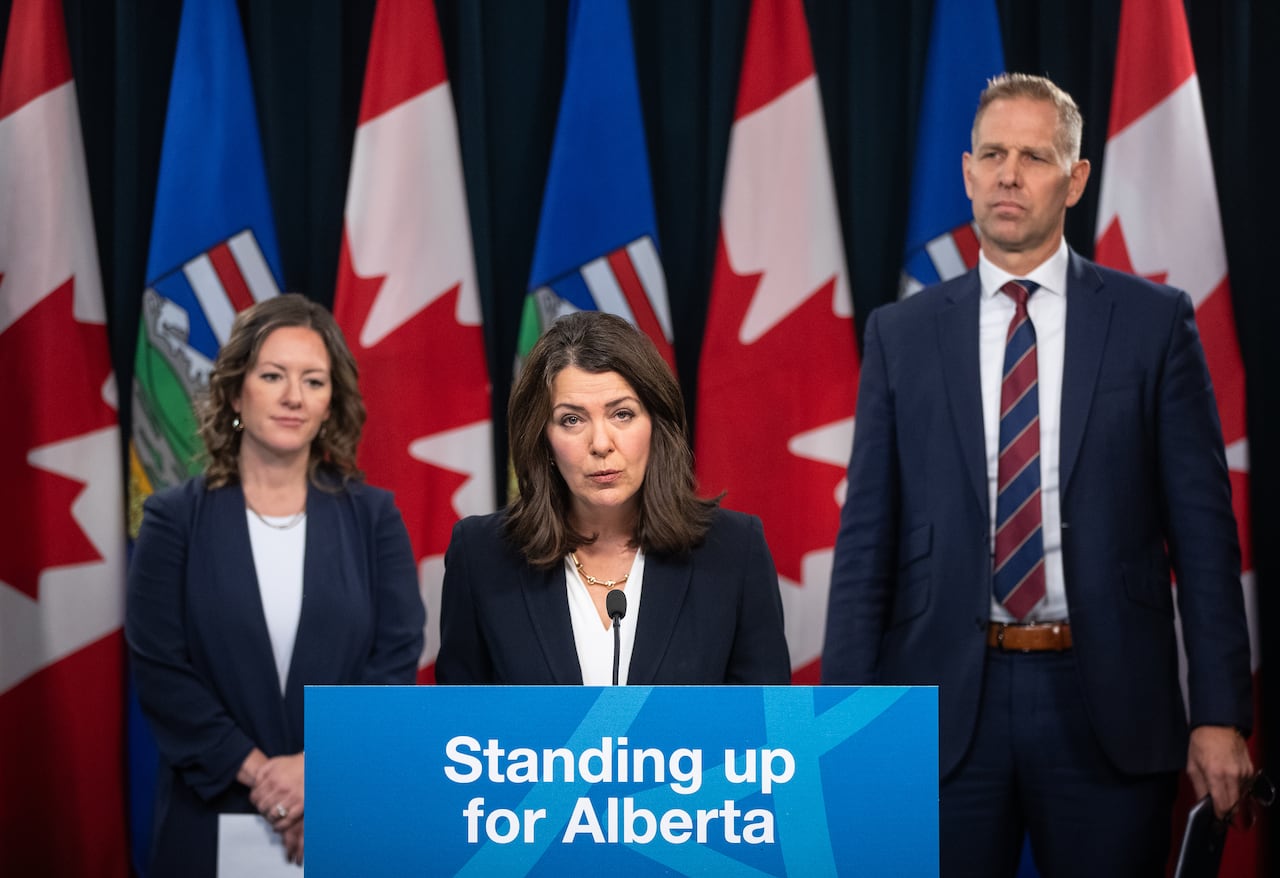 Two women and a man at podium that says 'Standing up for Alberta.'