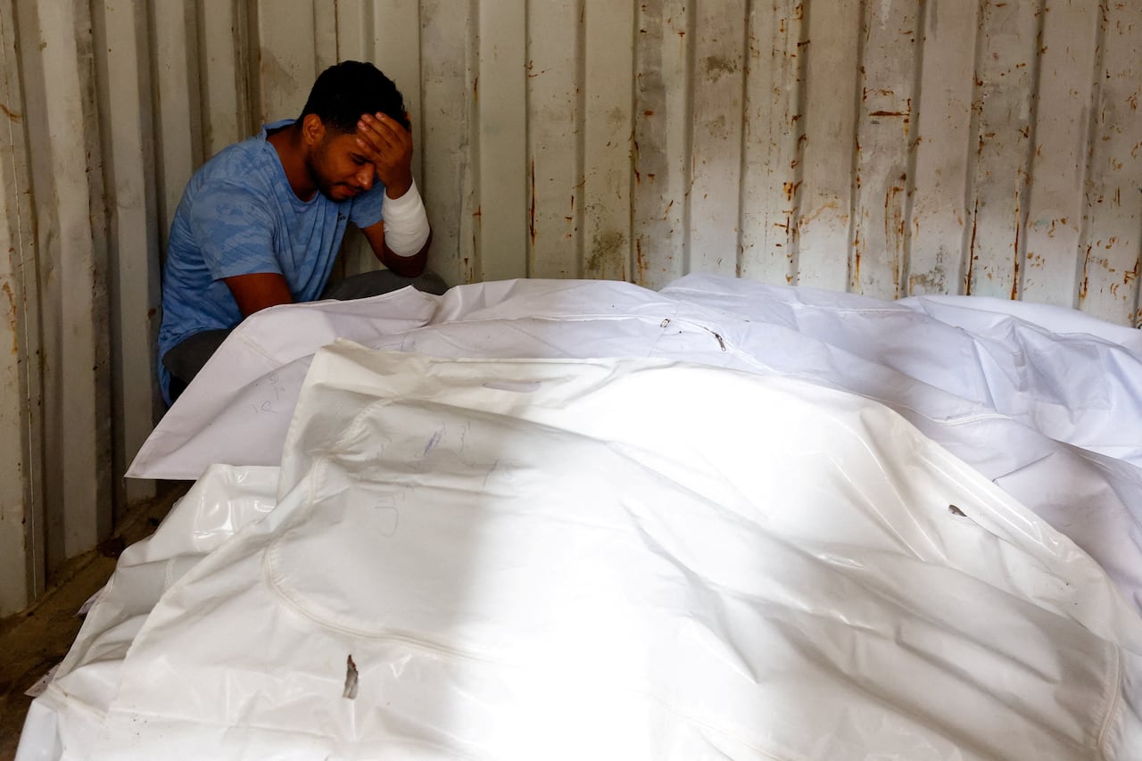 A man cries next to body bags.
