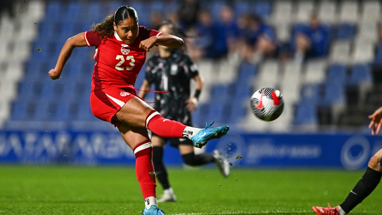 A female soccer player representing Canada kicks the ball with her right foot during a match.