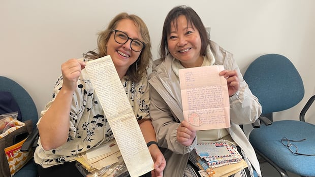 Two women hold up a stack of letters and envelopes smiling