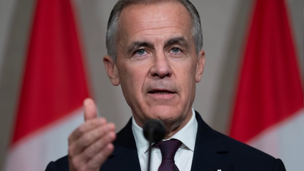 A man in a suit holds his hand up as he speaks at a microphone