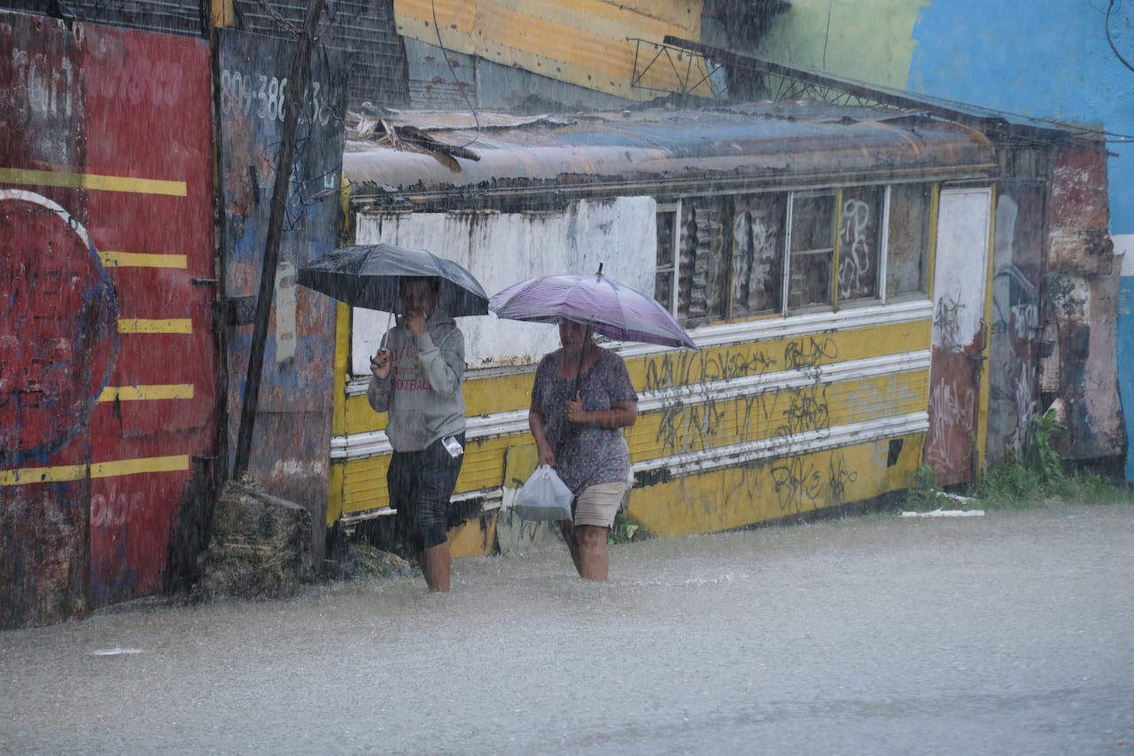 People with umbrellas wade through a flooded street during a rainstorm.