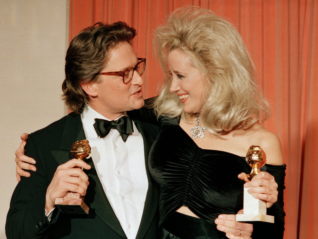 A man in a suit and a woman in black with their arms around each row on the red carpet, each holding a statuette and a globe 