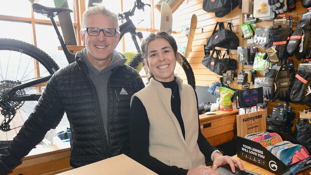 A man and a woman smile from behind the counter of a Jasper bike store. Two people smile from behind the counter of a Jasper bike store.