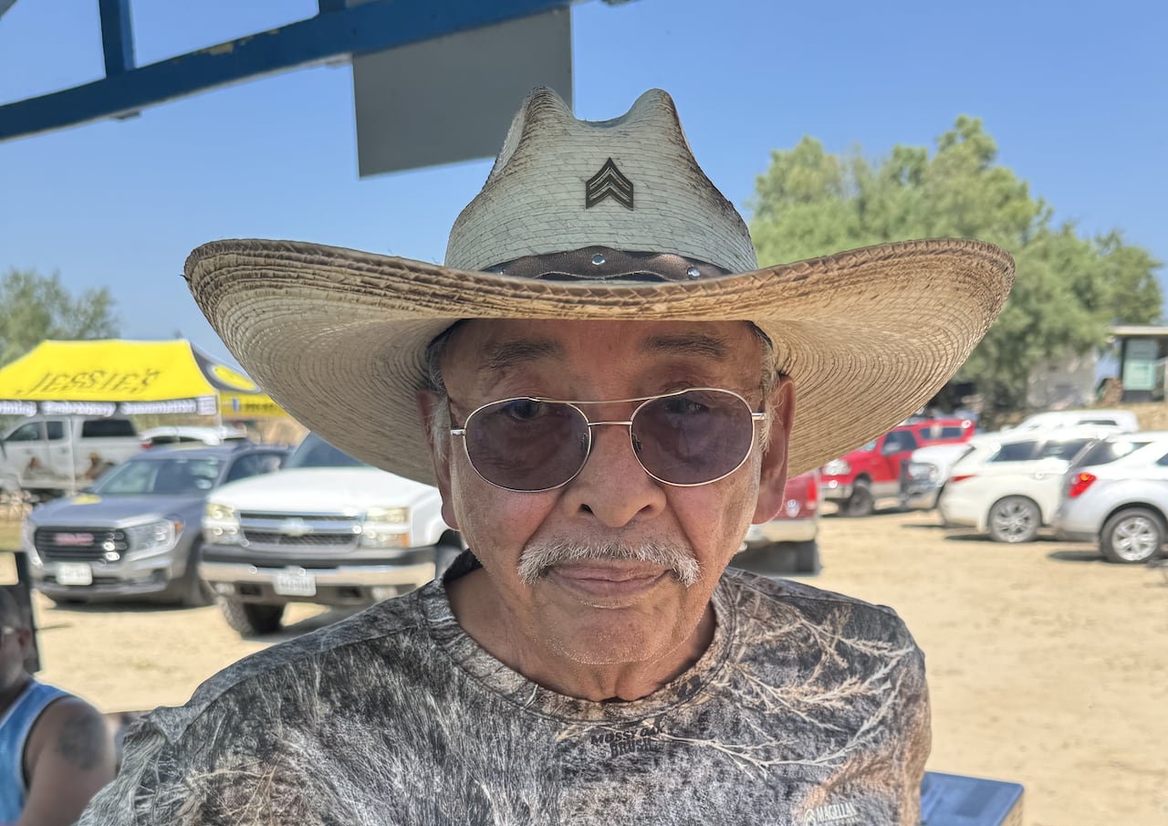 An old man in a cowboy hat poses for a photo