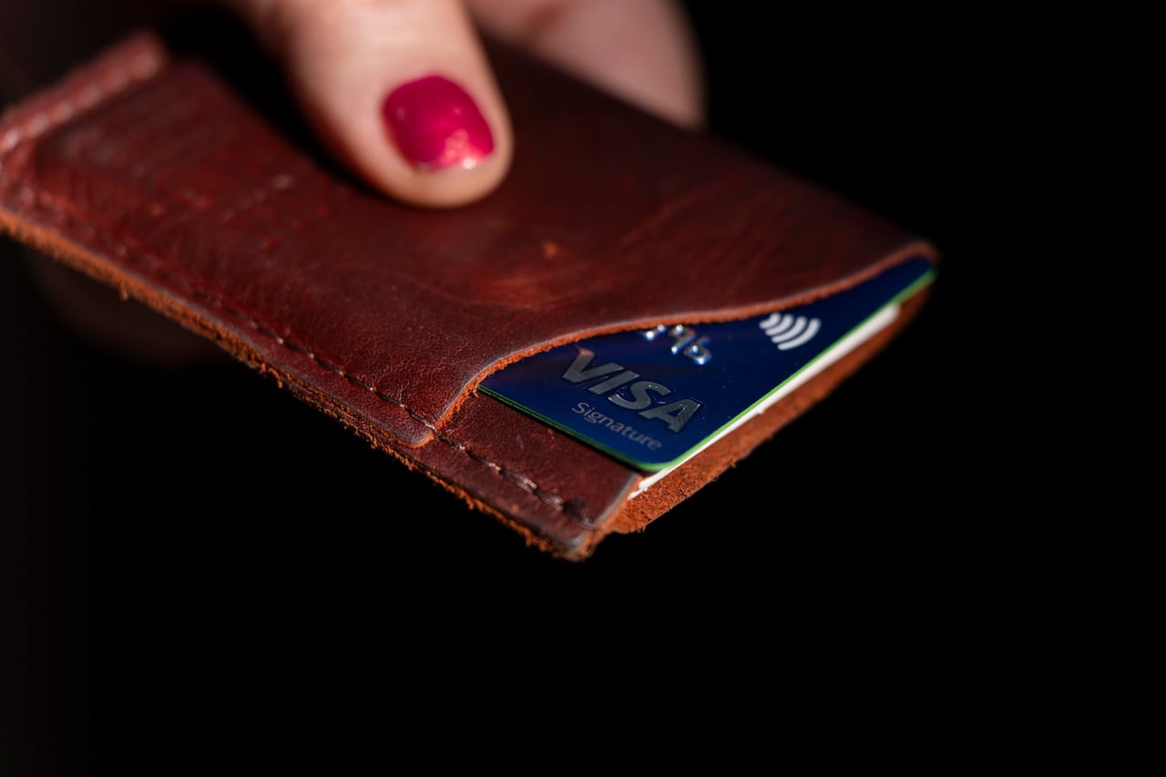 A person holds a wallet with a Visa card sticking out.