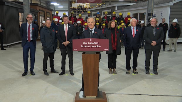 A man stands at a podium with a sign that reads "Buy Canadian"
