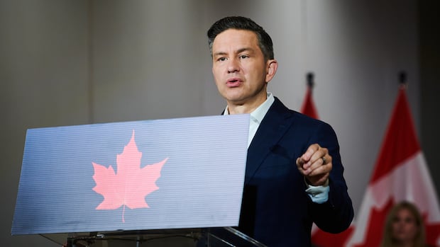 Pierre Poilievre stands at podium with Canadian flags and a woman in the background