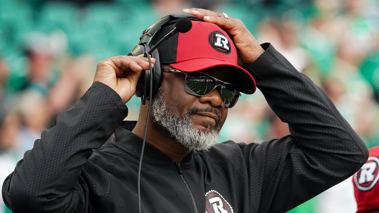 A man wearing a sweatshirt and a red baseball cap puts on a headset.
