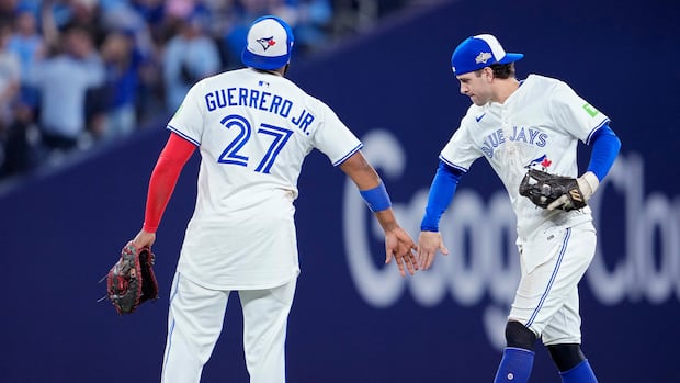 Two people in white uniforms high five on a field. 
