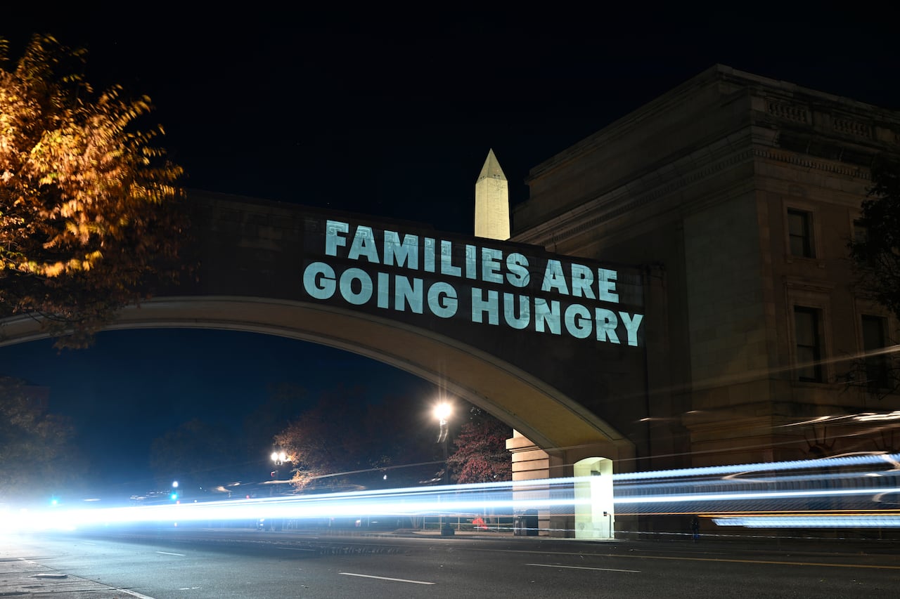 A message reading, 'Families are going hungry,' is projected onto the side of a building.