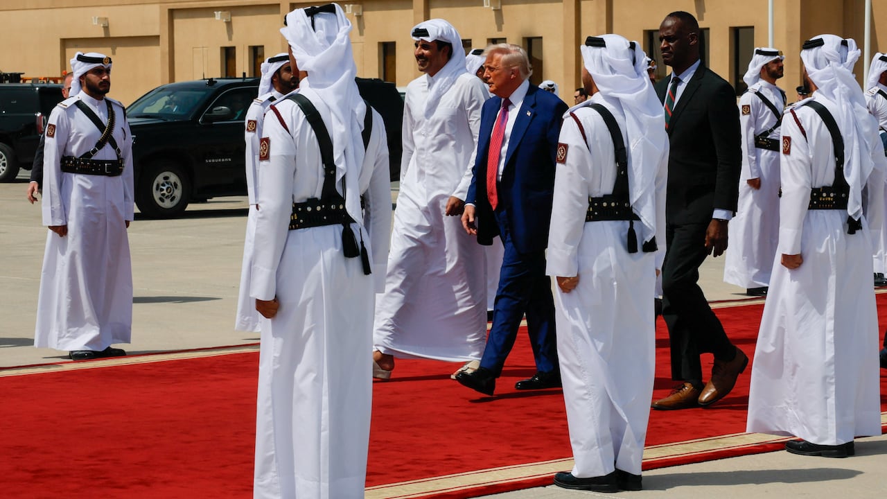 Men walk on a red carpet on an airport tarmac.