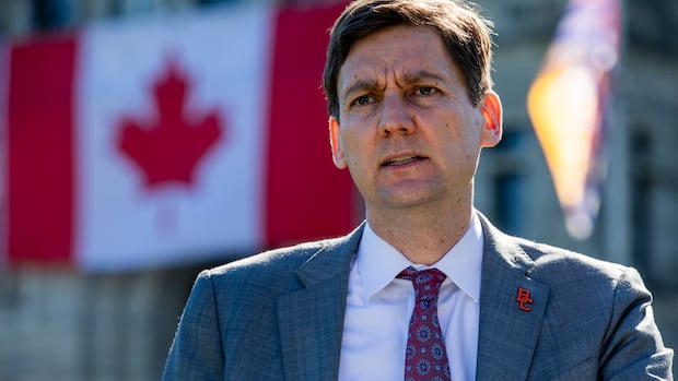 A man wearing a suit stands in front of a big Canada flag