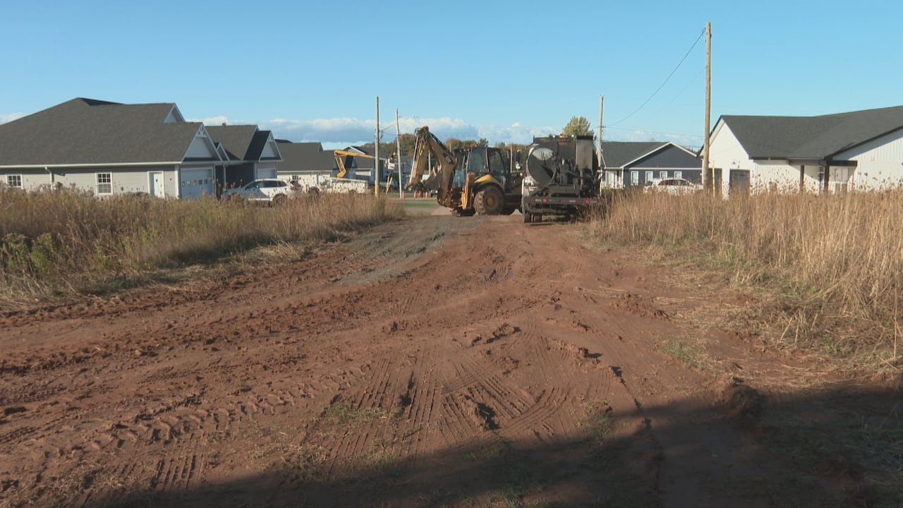 An unpaved road in a new residential development with construction equipment and several finished houses visible