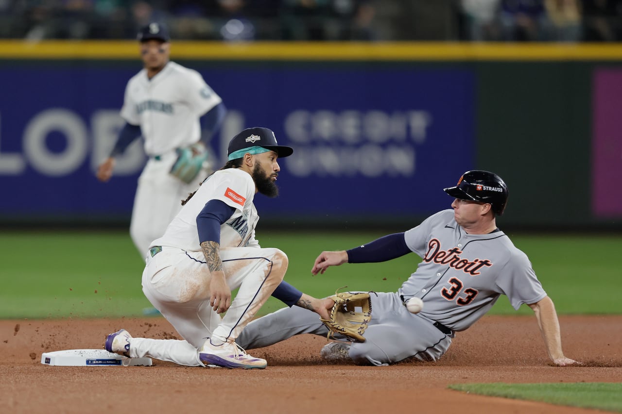 A baseball player slides into a base as an opposing player catches a ball.
