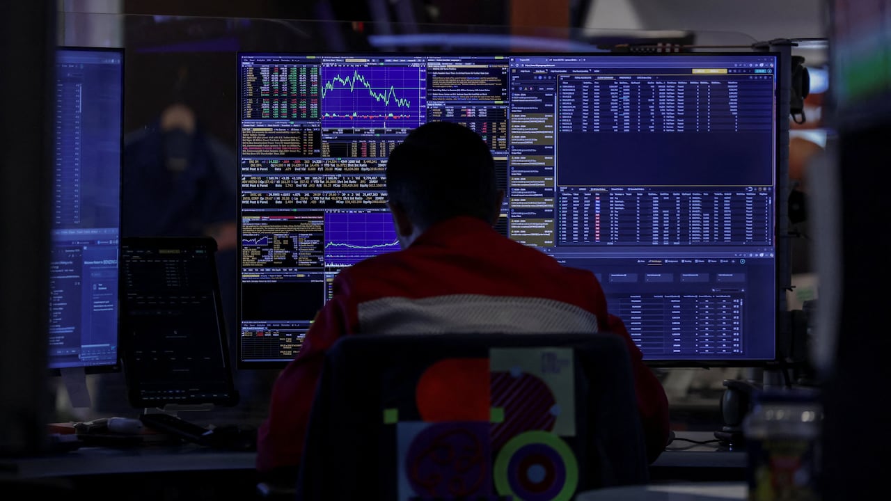 A trader is seated at a computer showing stock market graphics.