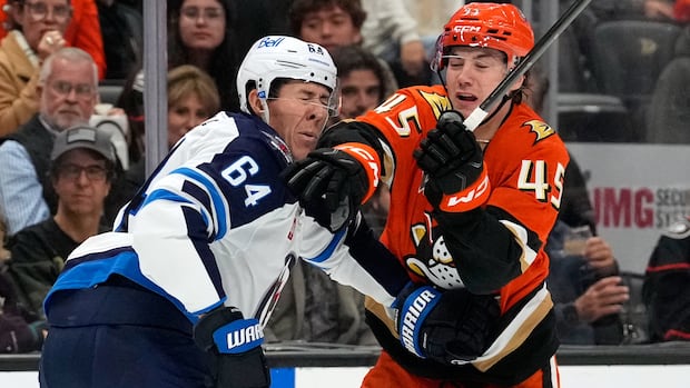 A hockey player in white and blue grimaces as he's hit in the face by a hockey player in orange.